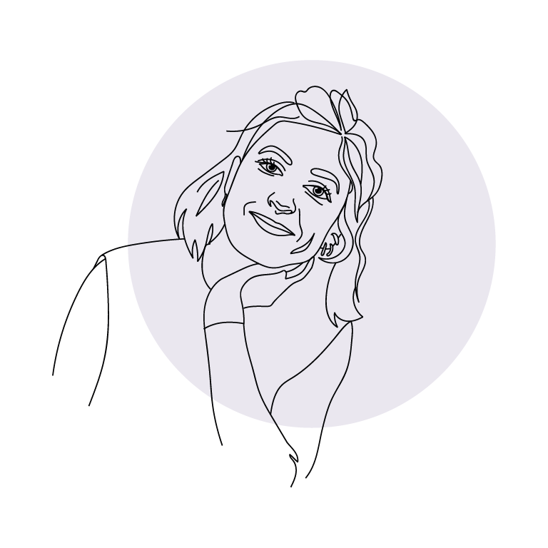 Ein Foto. Eine weiblich gelesene Person sitzt, der Kopf ist auf einer Hand abgestützt, sie lächelt in die Kamera.